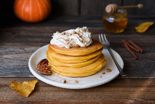 Pumpkin pancakes with whipped cream and cinnamon on old wooden table. 