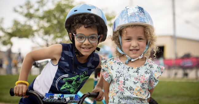 Two young children wearing bike helmets smiling.