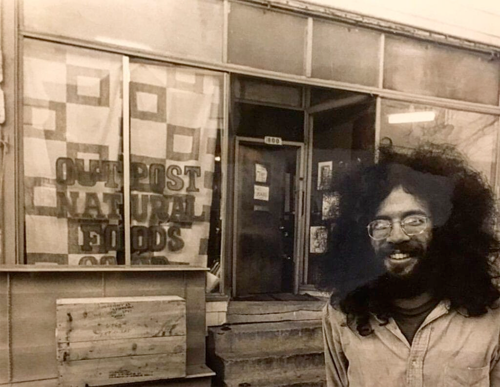 Black and white photo of a young Steve Pincus in front of Outpost Natural Foods Co-op.