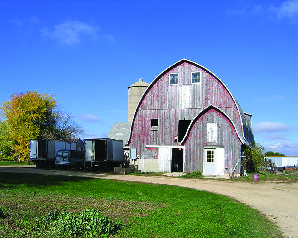 An old red barn in front of an almost cloudless blue sky.