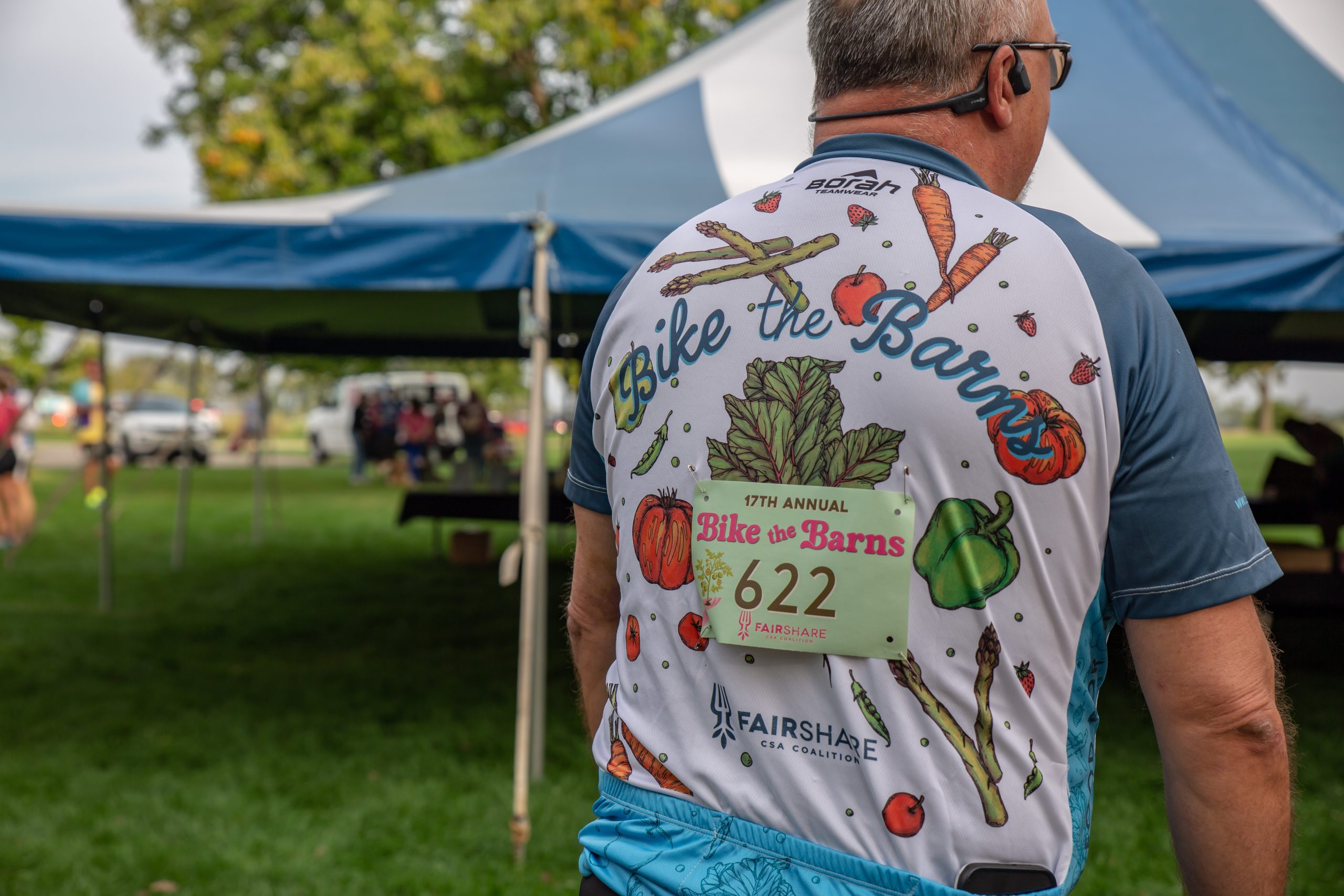 Person with a Bike the Barns shirt standing outdoors in front of a tent.