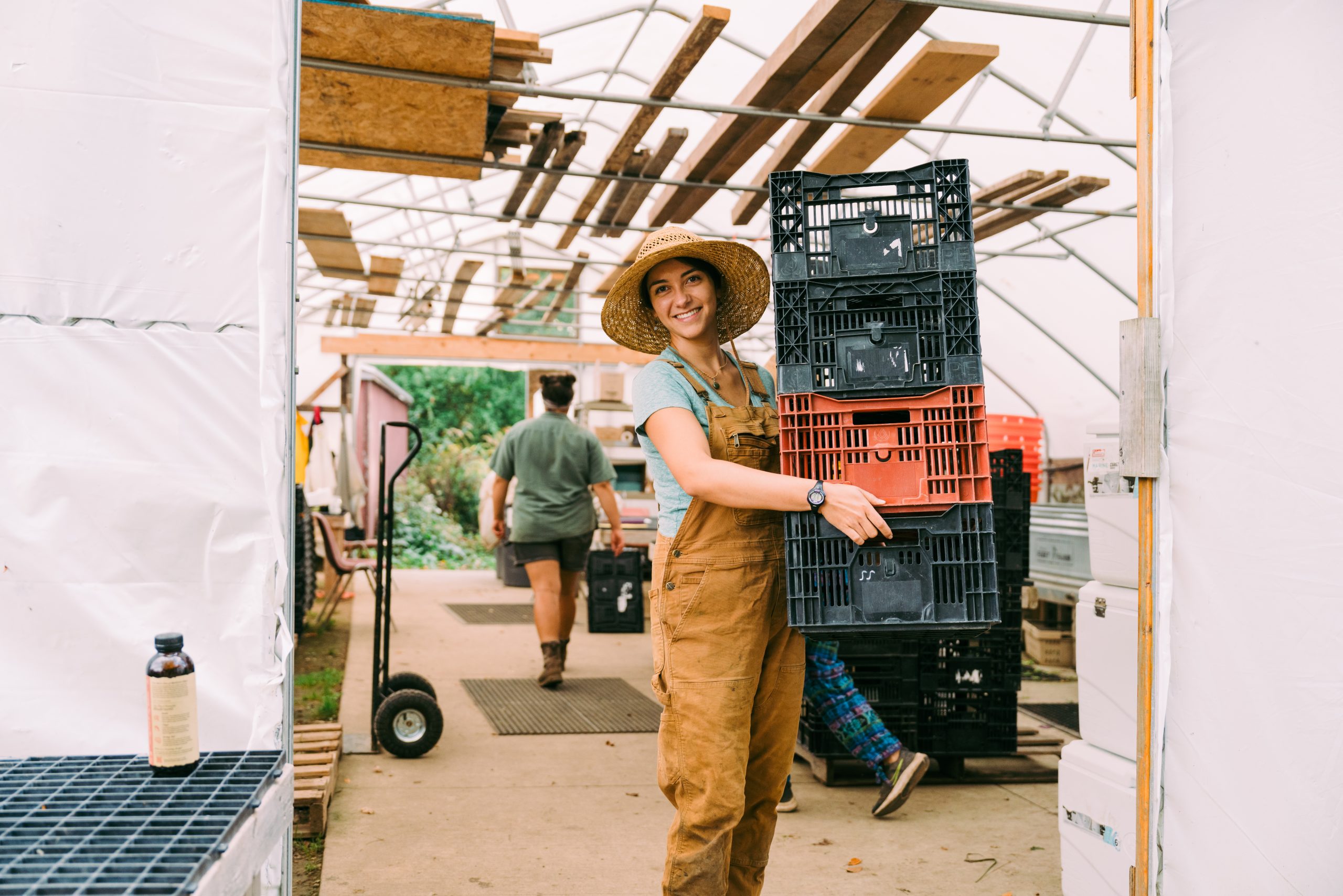 Woman farmer wearing a sun hat holding empty crates.