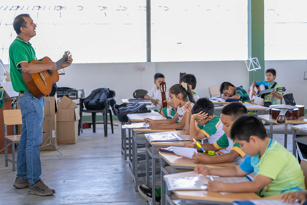 A man plays guitar in front of a classroom of young children.